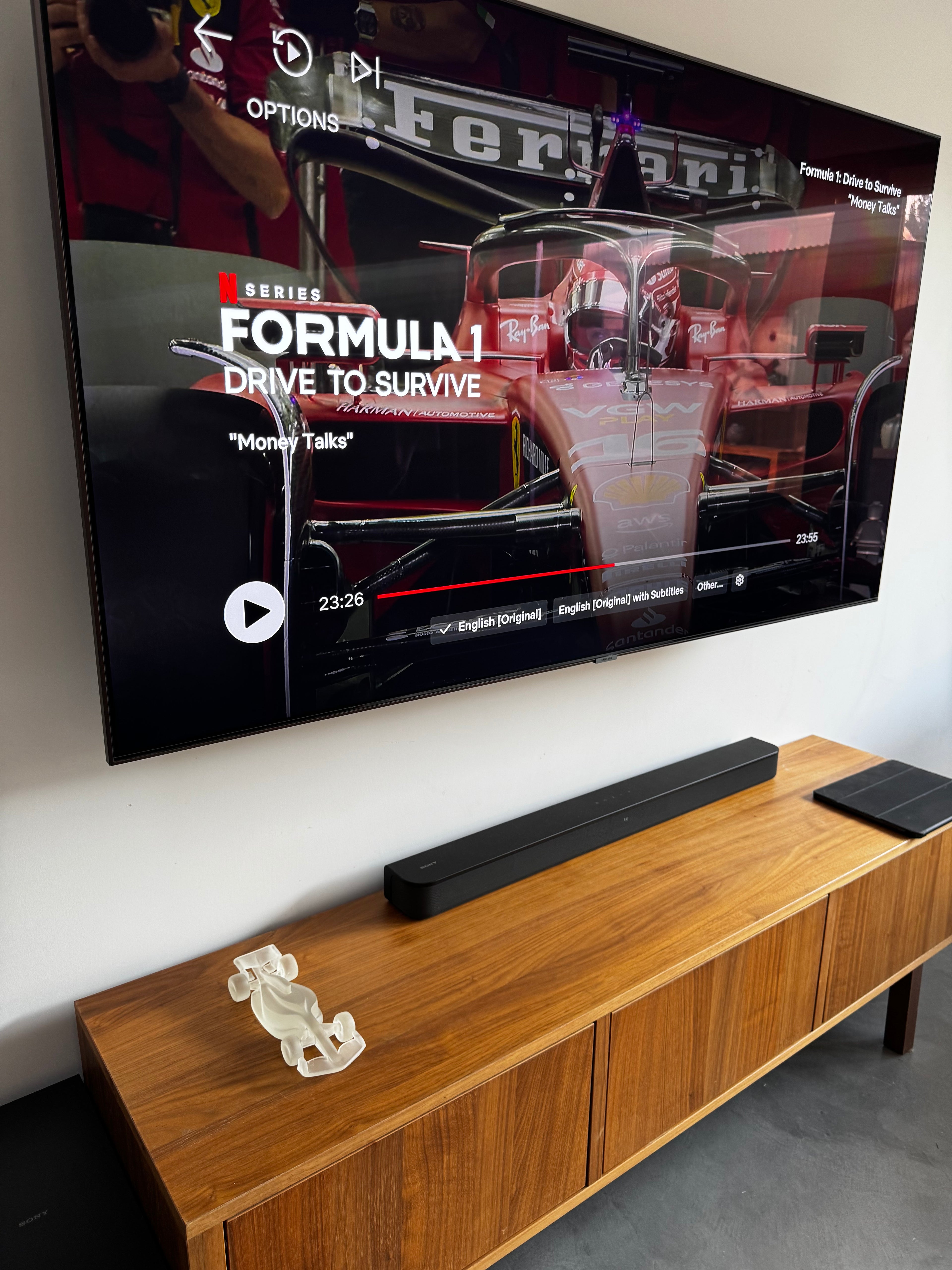 formula 1 drive to survive playing on tv in a living room with an f1 car sculpture on a tv console next to a soundbar.